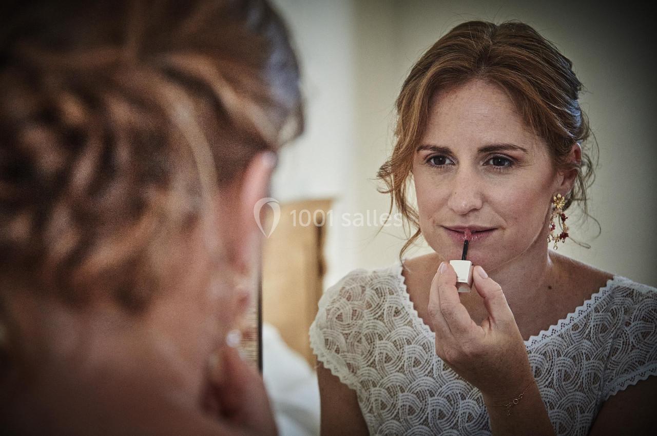 Une femme applique du rouge à lèvres devant un miroir, portant une robe blanche en dentelle.