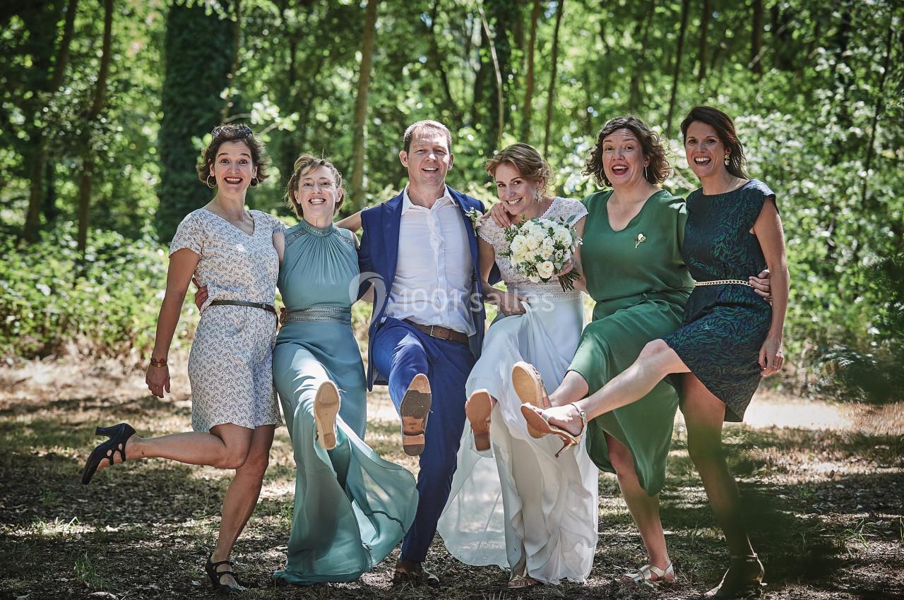 Un groupe de personnes souriantes lève une jambe en l'air dans un cadre boisé, lors d'une célébration.