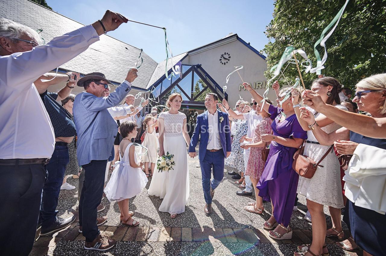 Un couple de mariés marche sous une haie d'honneur formée par des invités agitant des rubans colorés.