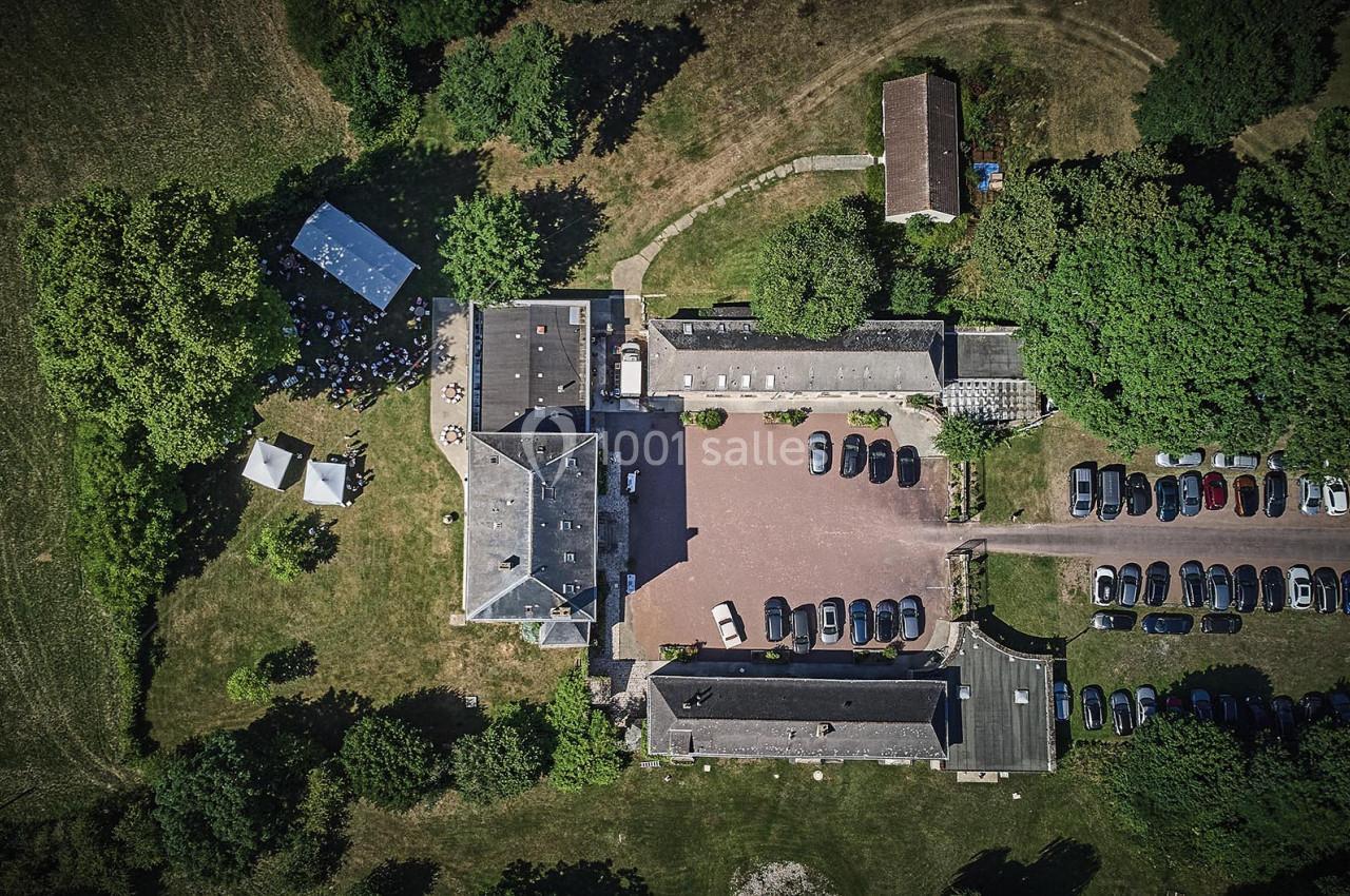 Vue aérienne d'un domaine avec bâtiments, parking rempli de voitures et espaces verts environnants.