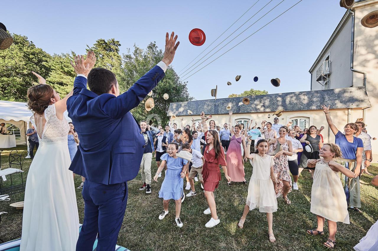 Un couple de mariés et des invités lancent des chapeaux en l'air lors d'une célébration en plein air.