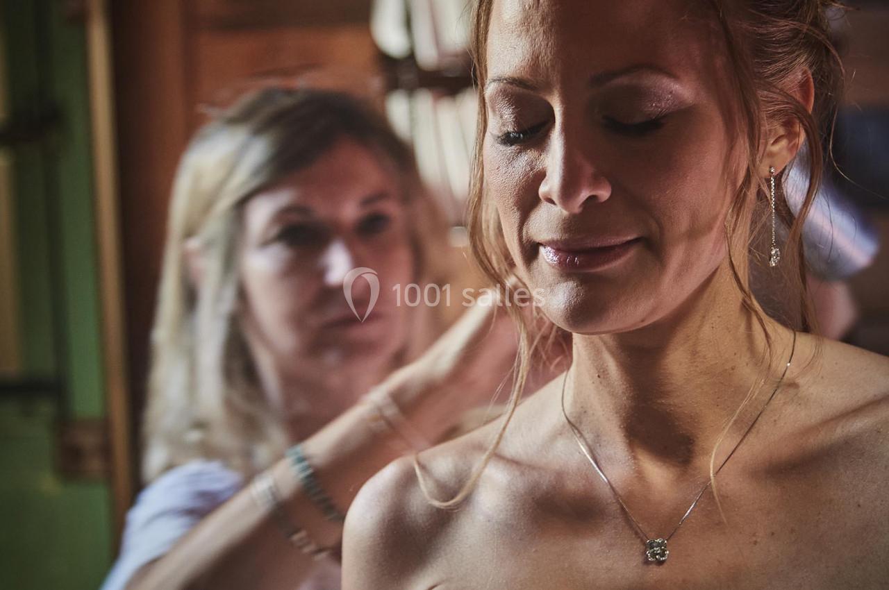 Une femme ajuste la coiffure d'une mariée portant une robe blanche dans une pièce en bois.