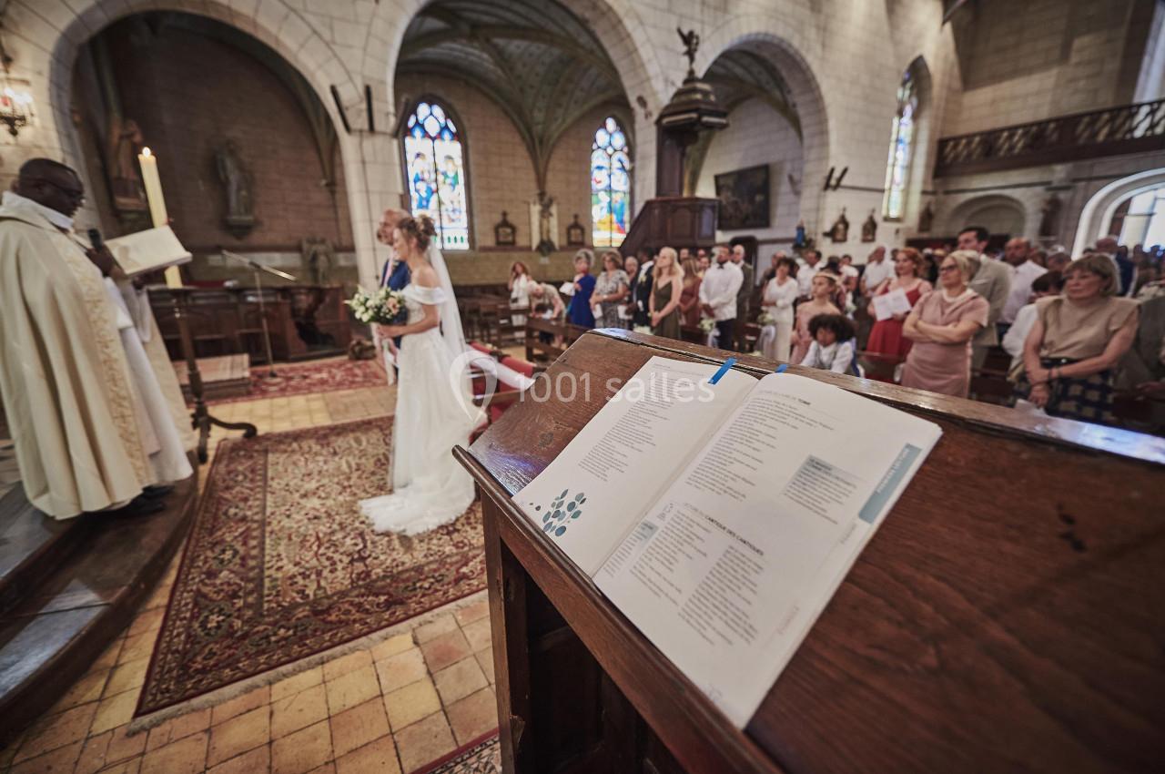 Un prêtre célèbre un mariage dans une église, avec des invités assis et un livre ouvert sur un pupitre au premier plan.