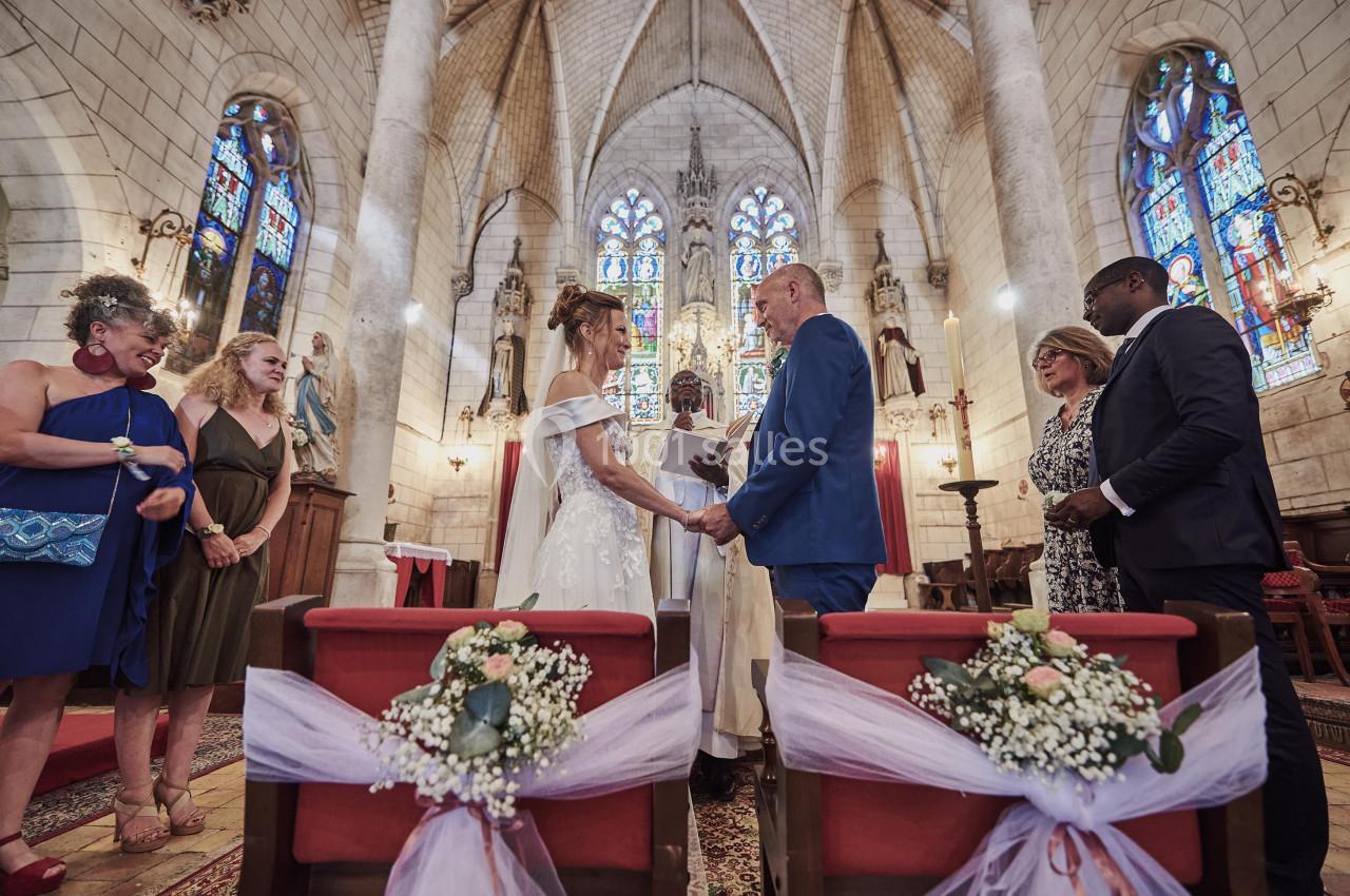 Un couple échange ses vœux de mariage dans une église, entouré de leurs proches et de décorations florales.