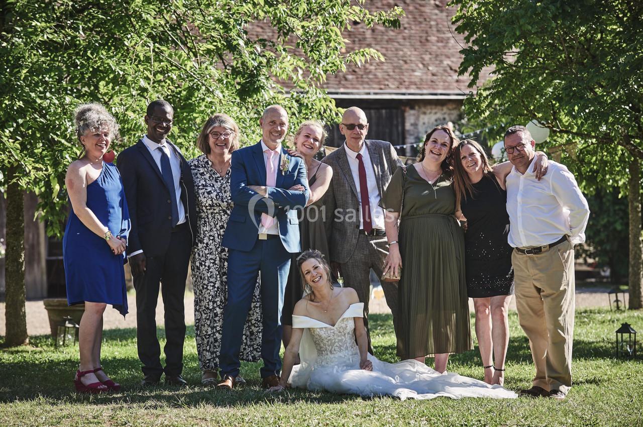 Un groupe de personnes pose dans un jardin, avec une mariée assise en robe blanche au premier plan.