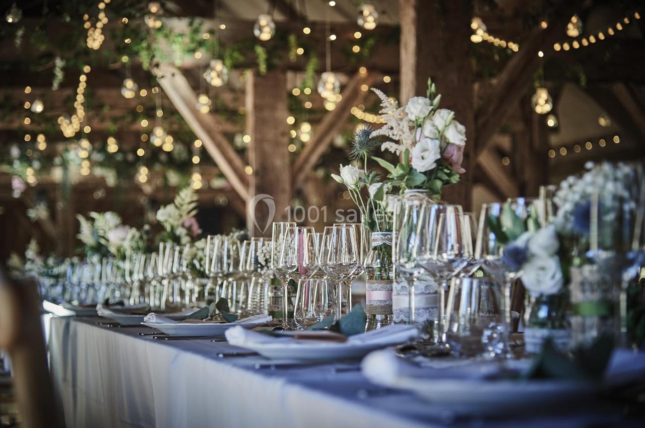 Table élégamment dressée avec nappes blanches, verres à pied et décorations florales dans une ambiance lumineuse.