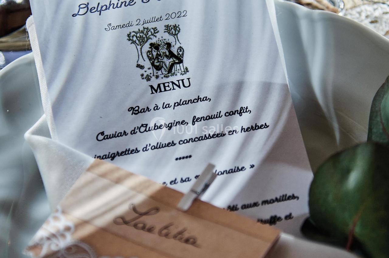 Menu de mariage posé sur une assiette blanche, accompagné d'un marque-place en bois décoré de dentelle.