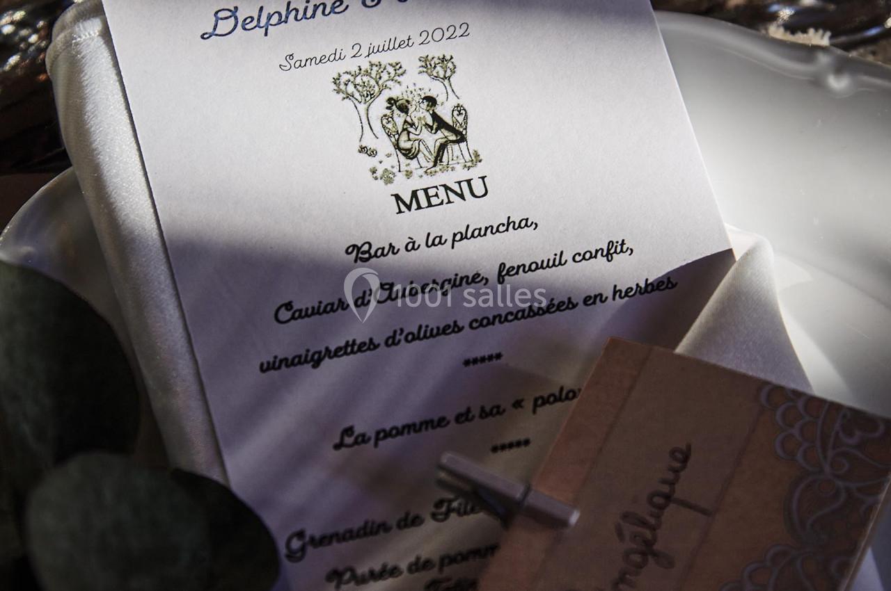 Menu de mariage imprimé sur une table, entouré de feuilles décoratives et d'une carte en papier kraft.