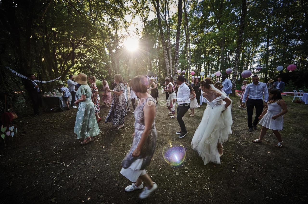 Personnes dansant en plein air dans une clairière boisée, décorée de guirlandes et de ballons, sous une lumière naturelle.