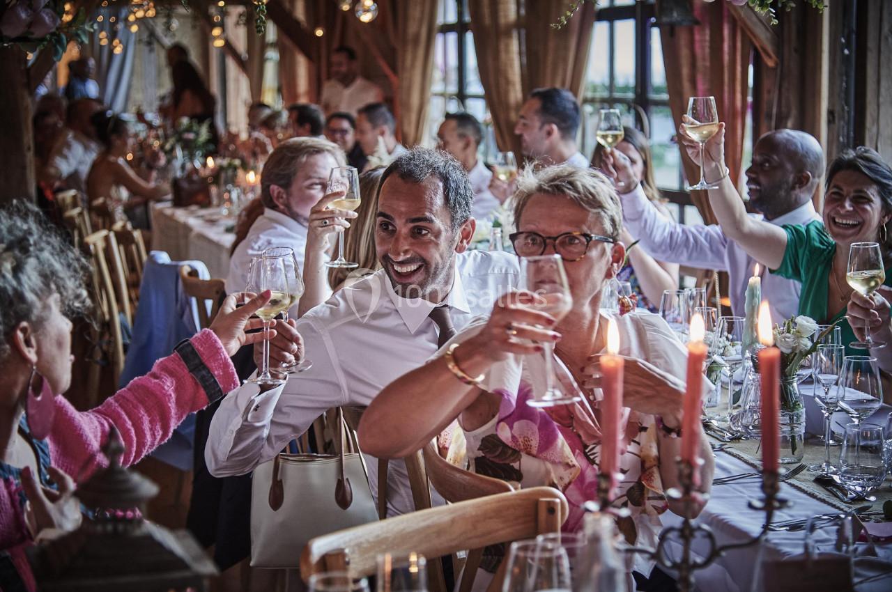 Des convives souriants lèvent leurs verres dans une salle décorée pour une fête ou un événement convivial.
