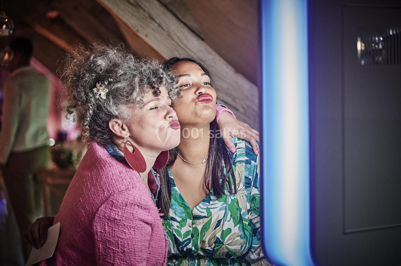 Deux femmes souriantes posent ensemble devant une borne photo dans un cadre intérieur chaleureux.