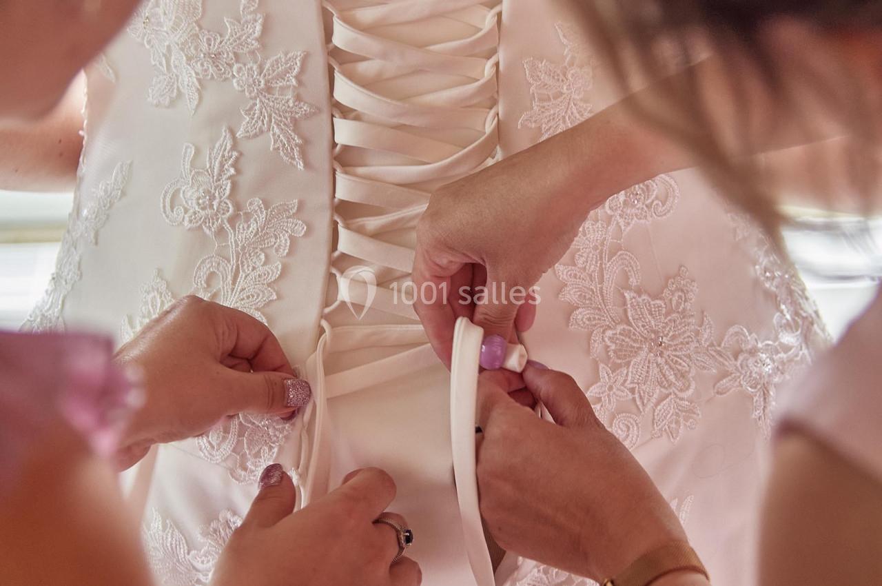 Deux personnes ajustent le laçage dans le dos d'une robe de mariée ornée de dentelle.