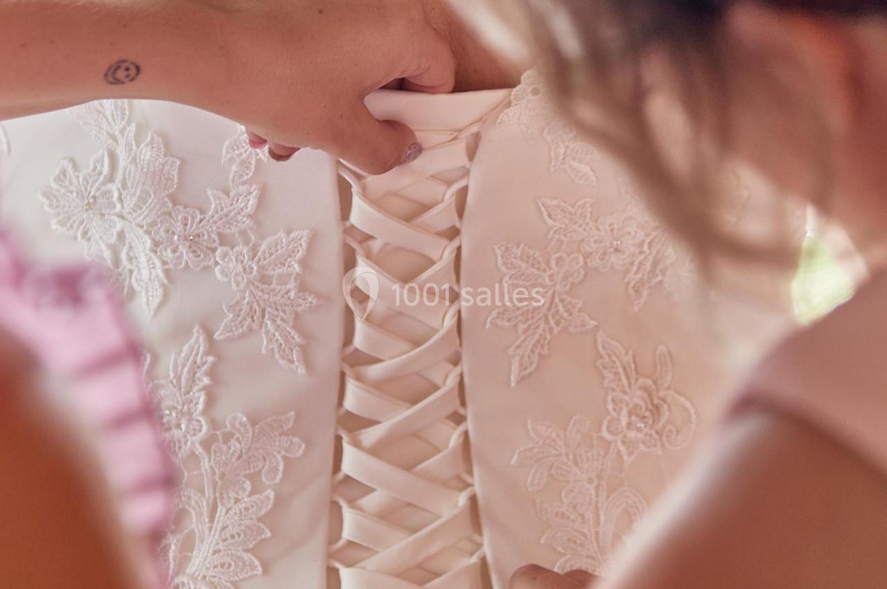 Deux personnes ajustent le laçage d'un corset de robe de mariée ornée de dentelle florale.