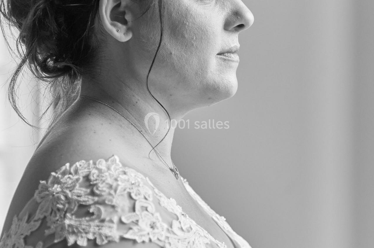Femme en robe de mariée regardant par une fenêtre, capturée en noir et blanc de profil.