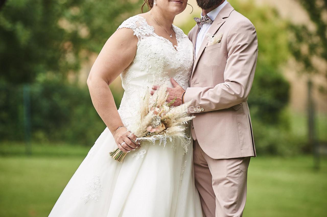 Un couple en tenue de mariage pose dans un jardin verdoyant, entouré d'arbres et d'herbe.