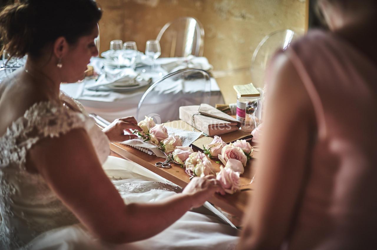 Une femme en robe blanche assemble des roses sur une table en bois, entourée de décorations de mariage.