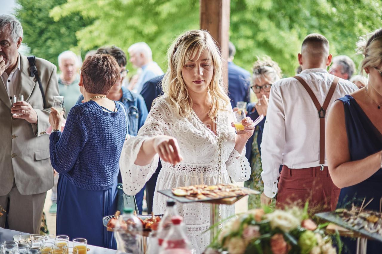 Une femme en robe blanche sert des amuse-bouches lors d'un événement en plein air entourée de convives.