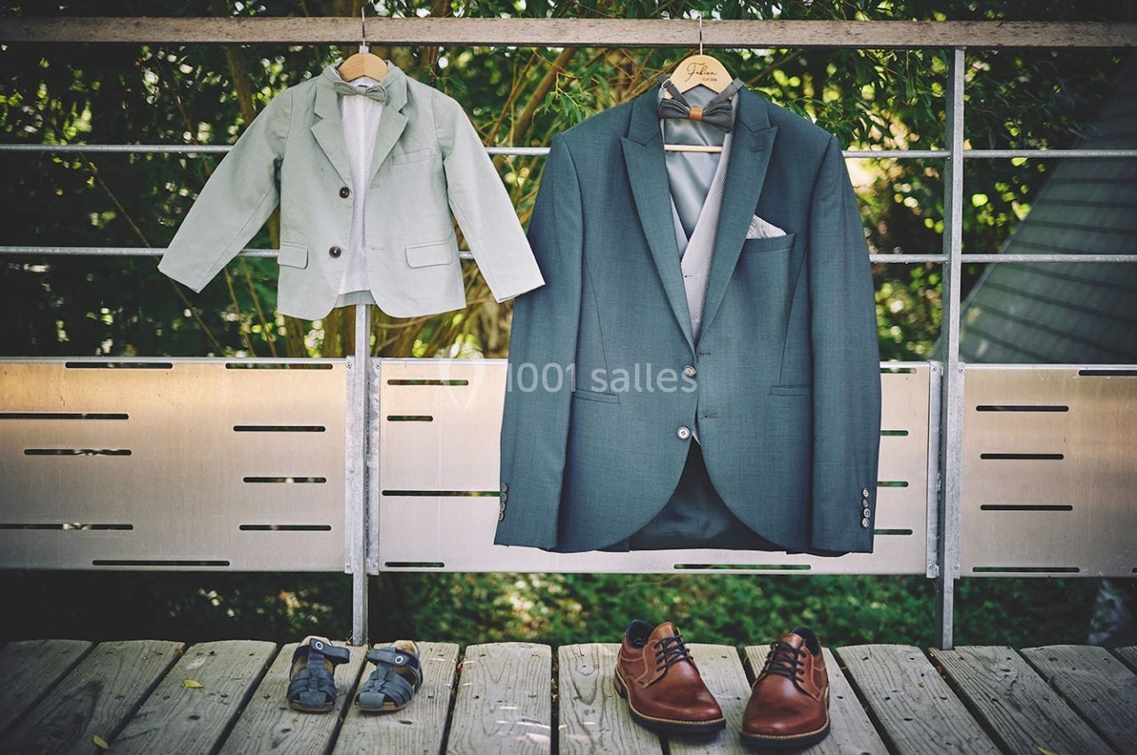 Deux costumes, un pour enfant et un pour adulte, suspendus à des cintres sur une rambarde en bois, avec des chaussures…