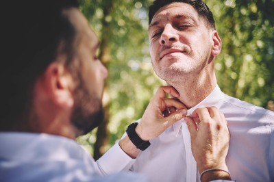 Un couple de mariés s'embrasse tendrement près d'un étang, entouré de verdure, la mariée tenant un bouquet coloré.