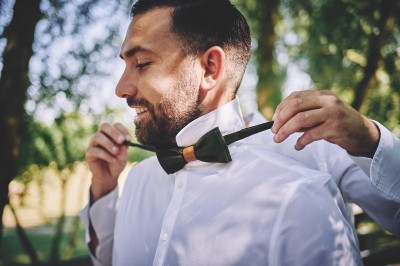 Un couple de mariés s'embrasse tendrement près d'un étang, entouré de verdure, la mariée tenant un bouquet coloré.