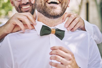 Un couple de mariés s'embrasse tendrement près d'un étang, entouré de verdure, la mariée tenant un bouquet coloré.