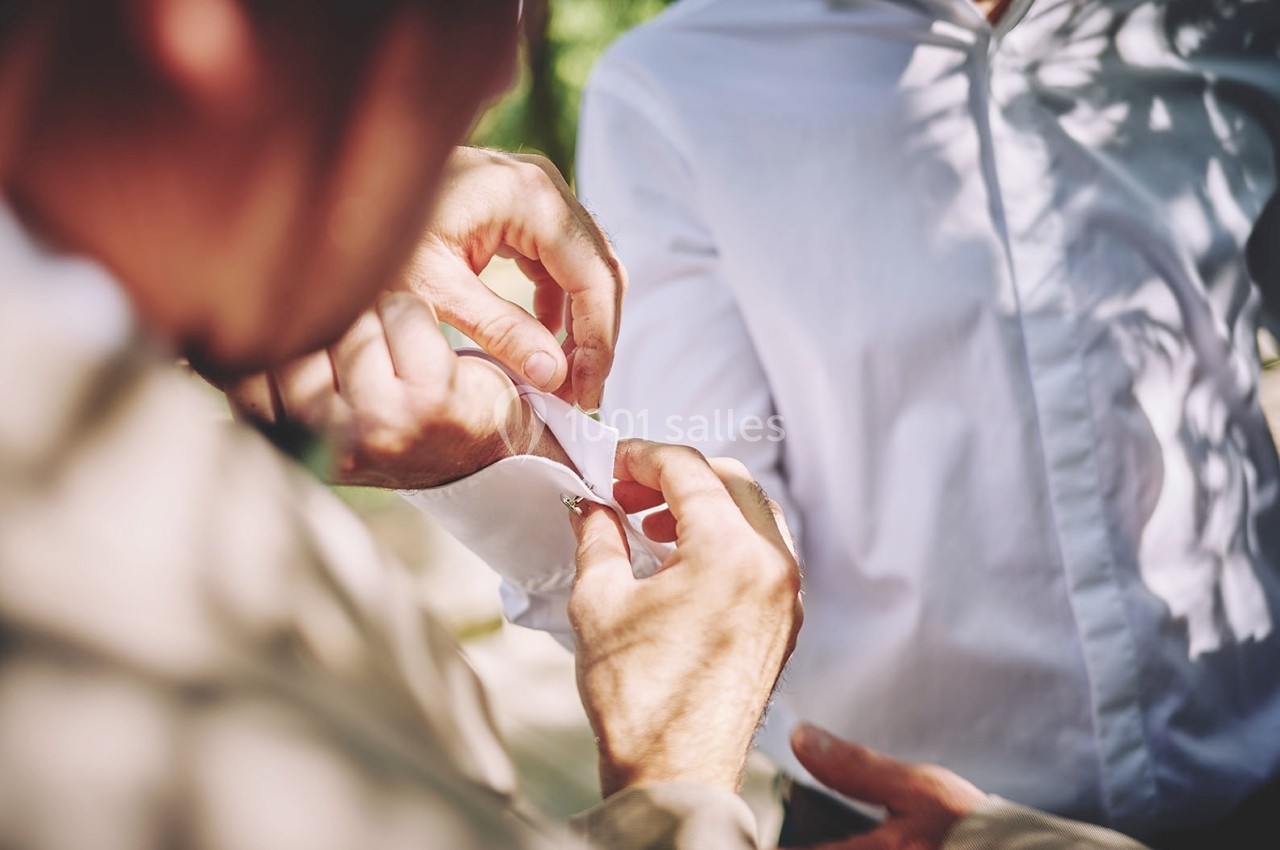 Une personne ajuste le bouton de manchette d'une chemise blanche portée par une autre personne en extérieur.
