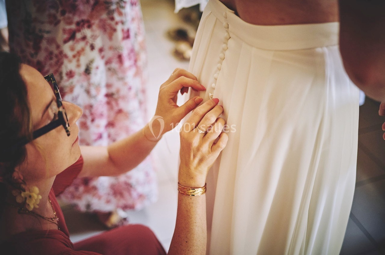 Une femme ajuste les boutons d'une robe blanche portée par une autre personne.