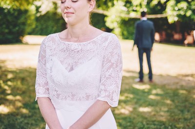 Un couple de mariés s'embrasse tendrement près d'un étang, entouré de verdure, la mariée tenant un bouquet coloré.