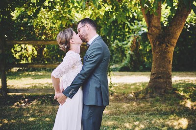 Un couple de mariés s'embrasse tendrement près d'un étang, entouré de verdure, la mariée tenant un bouquet coloré.