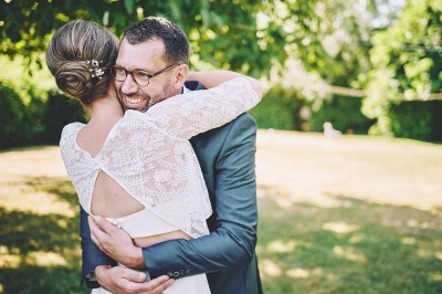 Un couple de mariés s'embrasse tendrement près d'un étang, entouré de verdure, la mariée tenant un bouquet coloré.