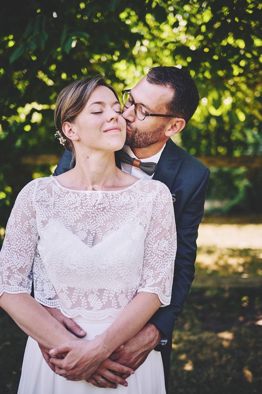 Un couple en tenue de mariage pose tendrement dans un jardin verdoyant.
