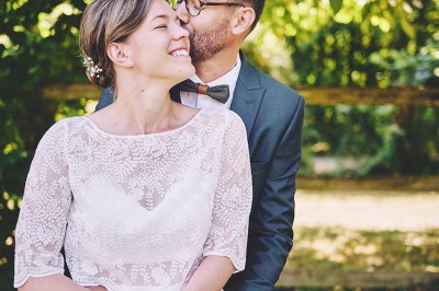 Un couple de mariés s'embrasse tendrement près d'un étang, entouré de verdure, la mariée tenant un bouquet coloré.