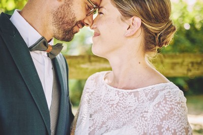 Un couple de mariés s'embrasse tendrement près d'un étang, entouré de verdure, la mariée tenant un bouquet coloré.
