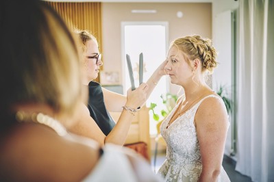 Un couple de mariés s'embrasse tendrement près d'un étang, entouré de verdure, la mariée tenant un bouquet coloré.