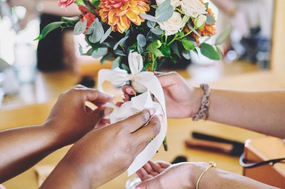 Un couple de mariés s'embrasse tendrement près d'un étang, entouré de verdure, la mariée tenant un bouquet coloré.