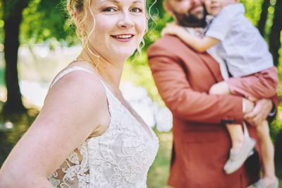 Un couple de mariés s'embrasse tendrement près d'un étang, entouré de verdure, la mariée tenant un bouquet coloré.