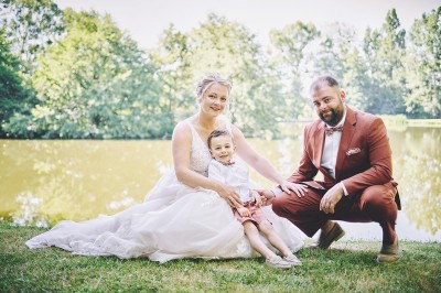 Un couple de mariés s'embrasse tendrement près d'un étang, entouré de verdure, la mariée tenant un bouquet coloré.