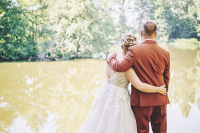 Un couple de mariés s'embrasse tendrement près d'un étang, entouré de verdure, la mariée tenant un bouquet coloré.