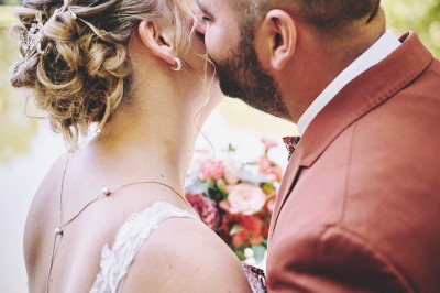 Un couple de mariés s'embrasse tendrement près d'un étang, entouré de verdure, la mariée tenant un bouquet coloré.