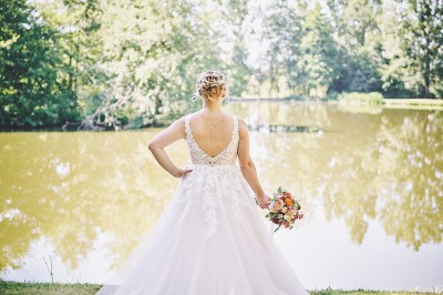 Un couple de mariés s'embrasse tendrement près d'un étang, entouré de verdure, la mariée tenant un bouquet coloré.