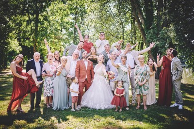 Un couple de mariés s'embrasse tendrement près d'un étang, entouré de verdure, la mariée tenant un bouquet coloré.