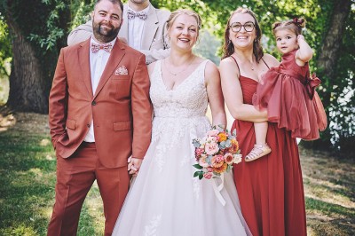 Un couple de mariés s'embrasse tendrement près d'un étang, entouré de verdure, la mariée tenant un bouquet coloré.