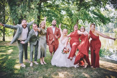 Un couple de mariés s'embrasse tendrement près d'un étang, entouré de verdure, la mariée tenant un bouquet coloré.