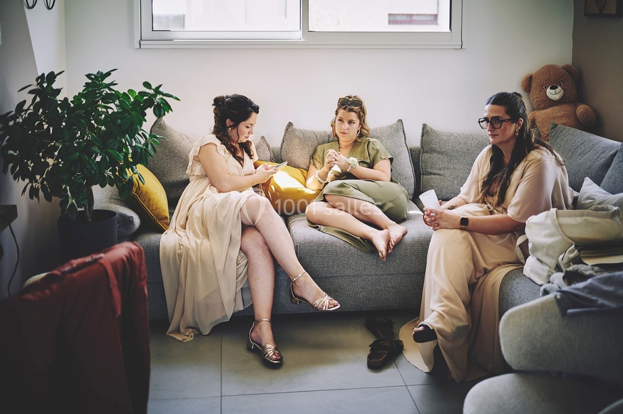 Trois femmes assises sur un canapé discutent et se détendent dans un salon lumineux avec des coussins et une plante.
