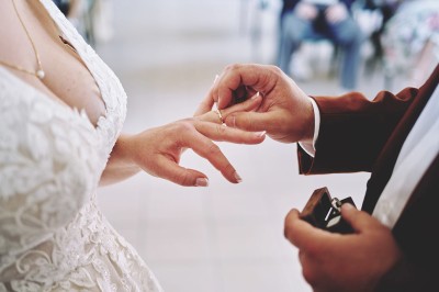 Un couple de mariés s'embrasse tendrement près d'un étang, entouré de verdure, la mariée tenant un bouquet coloré.