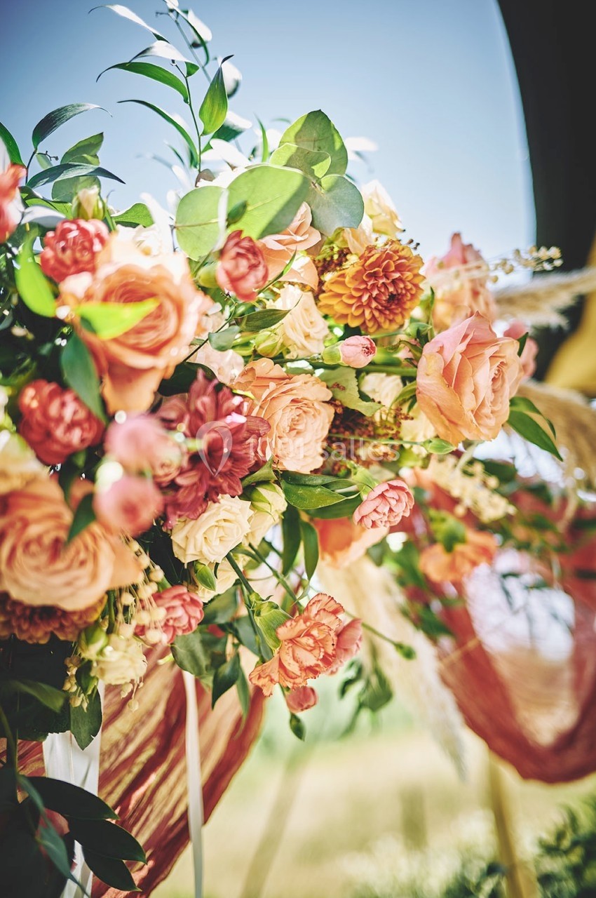 Arrangement floral coloré avec des roses, des dahlias et des feuillages verts, éclairé par une lumière naturelle.