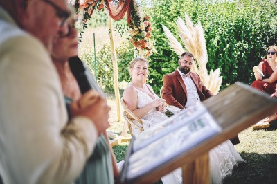 Un couple de mariés s'embrasse tendrement près d'un étang, entouré de verdure, la mariée tenant un bouquet coloré.