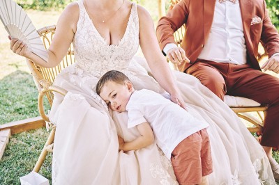 Un couple de mariés s'embrasse tendrement près d'un étang, entouré de verdure, la mariée tenant un bouquet coloré.