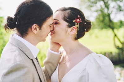 Un couple de mariés s'embrasse tendrement près d'un étang, entouré de verdure, la mariée tenant un bouquet coloré.