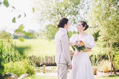 Un couple de mariés s'embrasse tendrement près d'un étang, entouré de verdure, la mariée tenant un bouquet coloré.